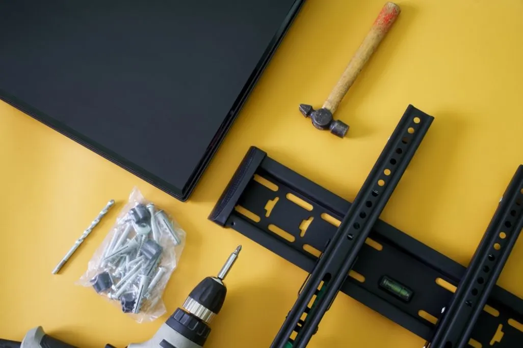 Montagematerial und Werkzeuge liegen neben einer Wandhalterung und einem Fernseher