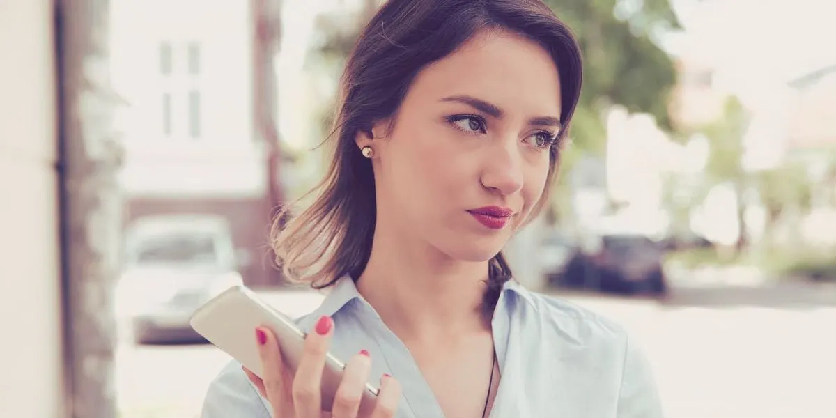 Frau hält skeptisch ihr Smartphone in der Hand und steht im Freien.