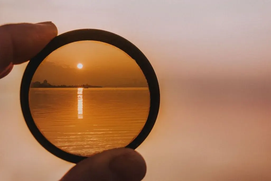 Daumen und Zeigefinger halten einen Filter vor einem rot-orangen Sonnenuntergang über dem Meer.