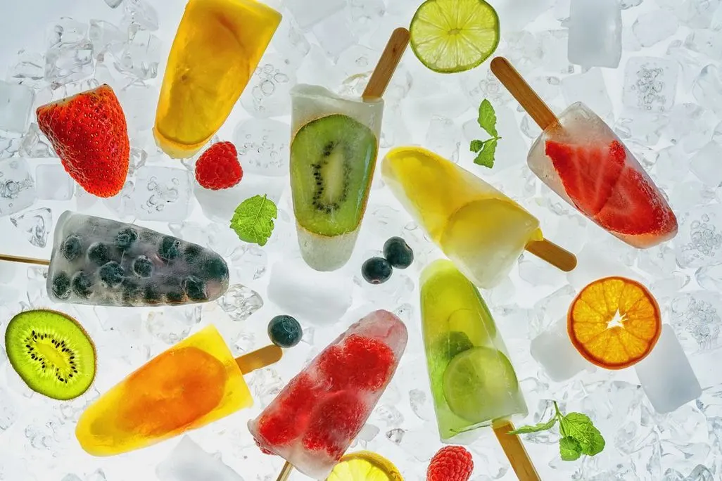 Verschiedene selbstgemachte Eis am Stiel mit Früchten auf Eiswürfeln angerichtet.