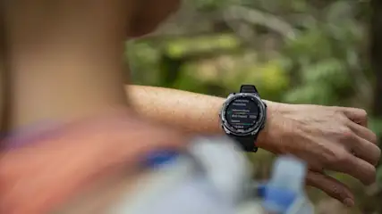 Person im Wald trägt Sportuhr mit Trainingsdaten am Handgelenk.