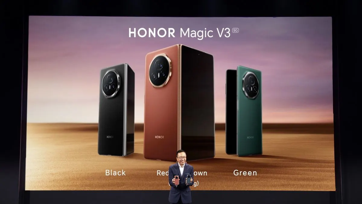 Ein Mann präsentiert auf einer Bühne drei HONOR Magic V3 5G Smartphones in Schwarz, Rotbraun, Grün auf einem Bildschirm und hält zwei Modelle.