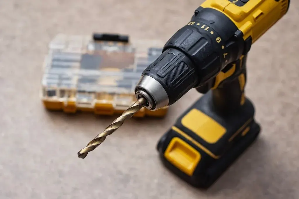 Gelb-schwarzer Akku-Bohrschrauber mit Spiralbohrer und unscharfem Werkzeugkoffer auf grauem Untergrund