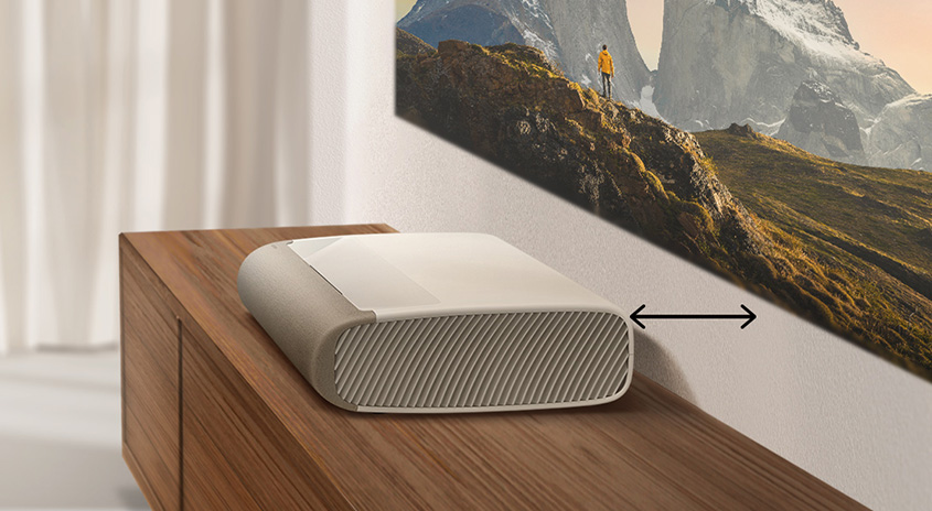 Ein beiger Projektor steht auf einem Holzschrank und projiziert ein Bergpanorama an die Wand.