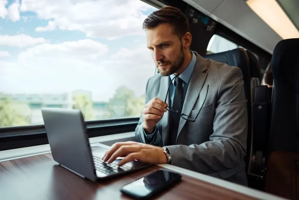 Mann sitzt im Zug mit Laptop und Handy