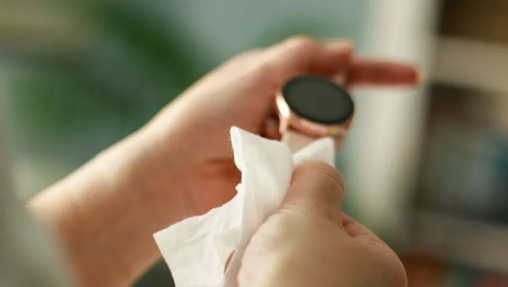 Hände reinigen eine roségoldene Smartwatch mit dunklem Bildschirm und einem weißen Tuch.