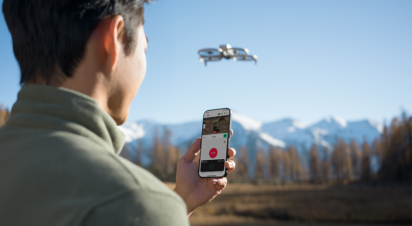 Eine Drohne fliegt im Freien, gesteuert mit einem Smartphone vor einer Bergkulisse.