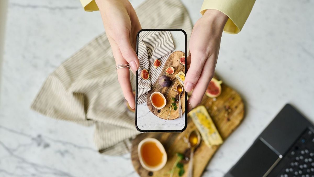Hände halten ein Smartphone und fotografieren einen gedeckten Tisch mit Feigen und Käse.