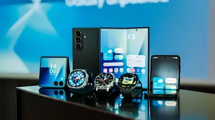 Drei schwarze Samsung Galaxy Z Fold 7 und Flip 7 Smartphones, sowie drei Samsung Galaxy Watches auf glänzender schwarzer Fläche vor blauem Hintergrund.