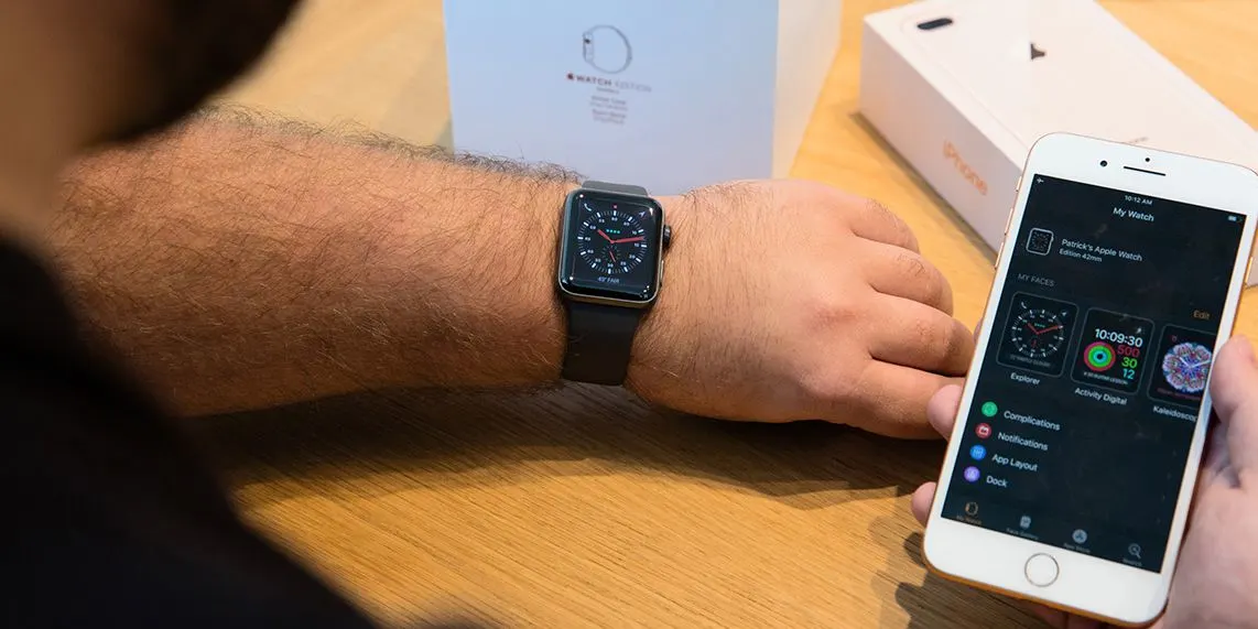 Person trägt eine schwarze Smartwatch und hält ein Smartphone mit geöffneter App.