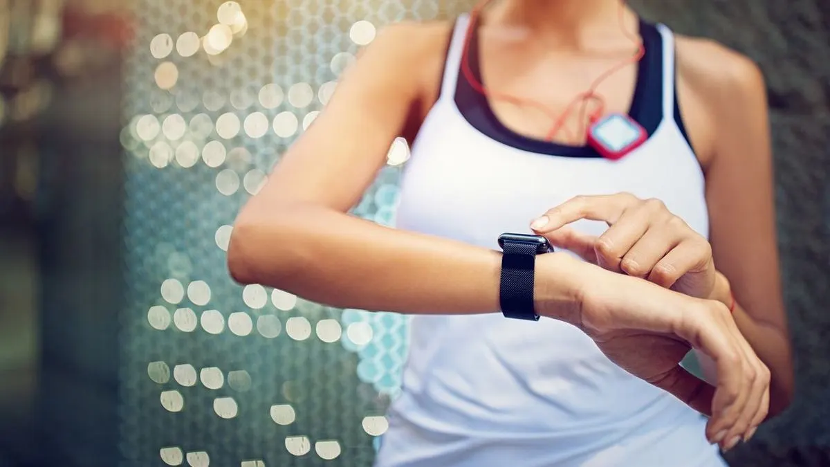 Frau in weißem Sporttop mit Fitnesssensor bedient ihre schwarze Smartwatch.