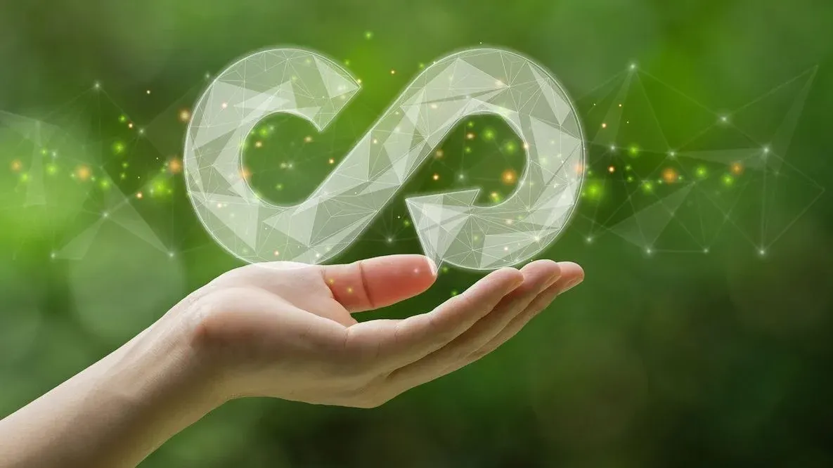 Hand hält leuchtendes, polygonales Unendlichkeitszeichen vor verschwommenem grünem Hintergrund mit vernetzten Lichtpunkten.