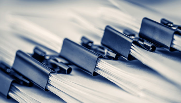 Reihe von Papierstapeln, die mit dunklen Metallklammern zusammengehalten werden, auf einem hellen Untergrund.