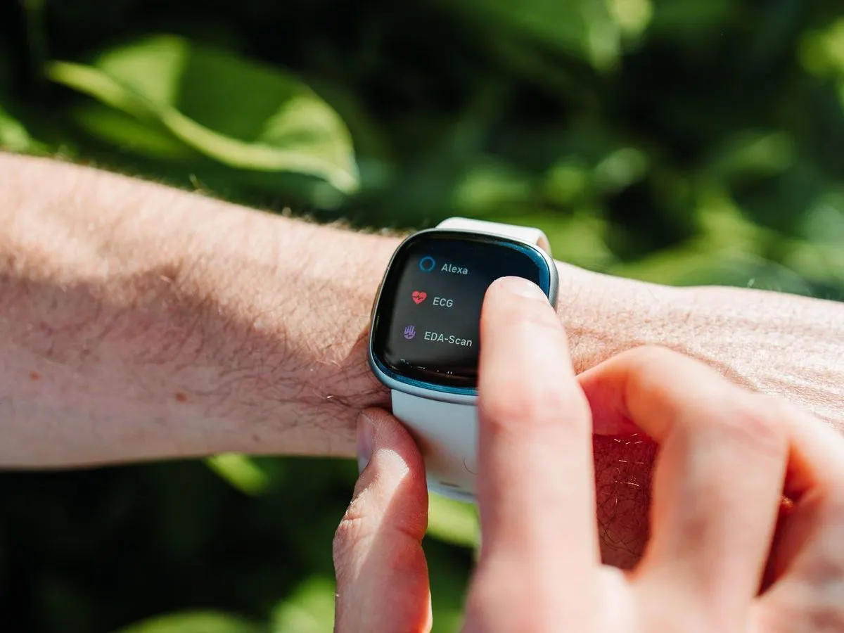 Person bedient eine Smartwatch mit weissem Armband im Freien