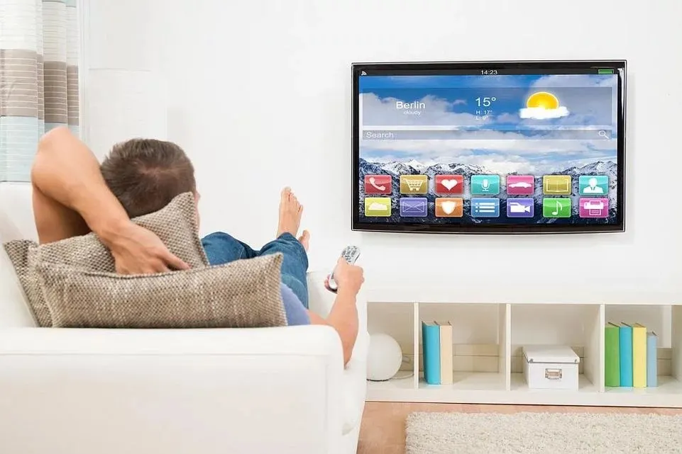 Mann liegt auf einem Sofa und steuert mit einer Fernbedienung einen Smart TV