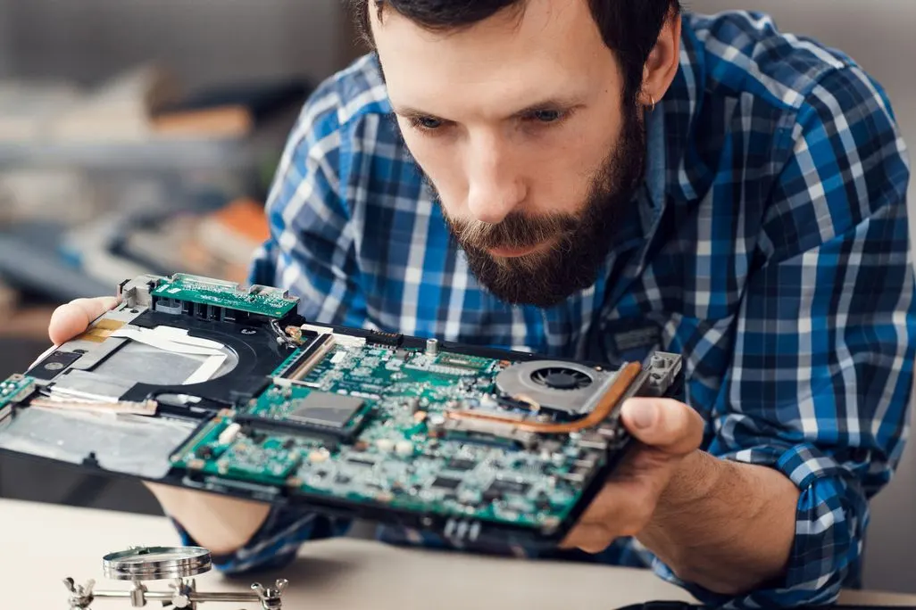 Mann in kariertem Hemd untersucht geoeffnetes Laptop-Mainboard