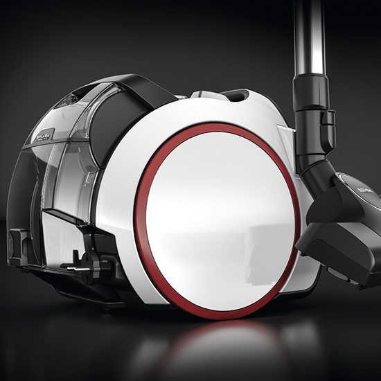 Detailaufnahme eines Staubsaugers mit transparentem Behälter, weißem Gehäuse und rotem Akzentring auf dunklem Hintergrund.