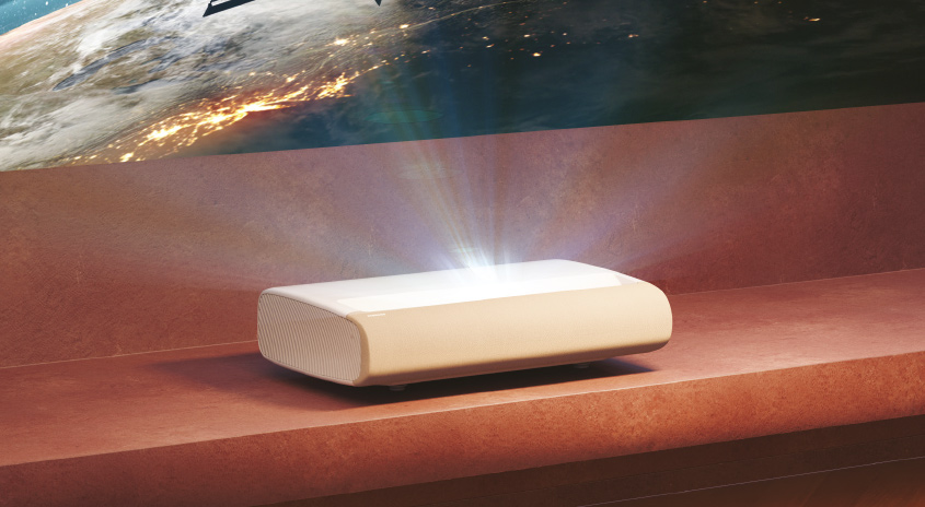 Ein weißer Projektor auf einer braunen Oberfläche strahlt Licht auf eine Wand mit einer Erdkugel.