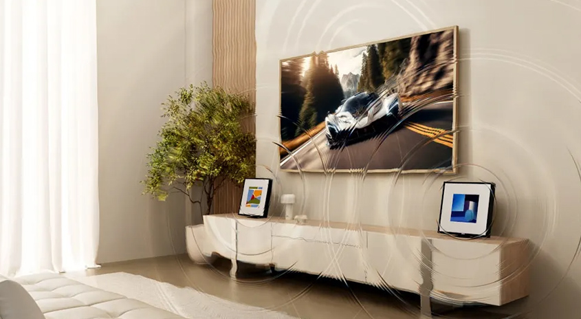 Ein Wohnzimmer mit einem Fernseher, der ein Auto auf einer Straße zeigt, über einem weißen Sideboard. Pflanzen und Bilderrahmen sind auch vorhanden.