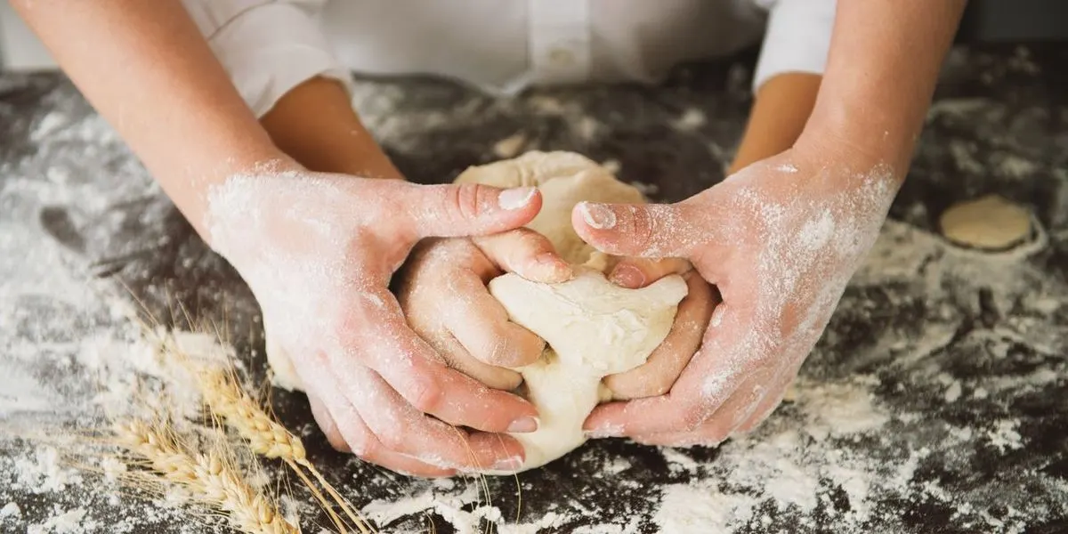 Eine Person knetet einen Teig auf einer bemehlten Arbeitsfläche.