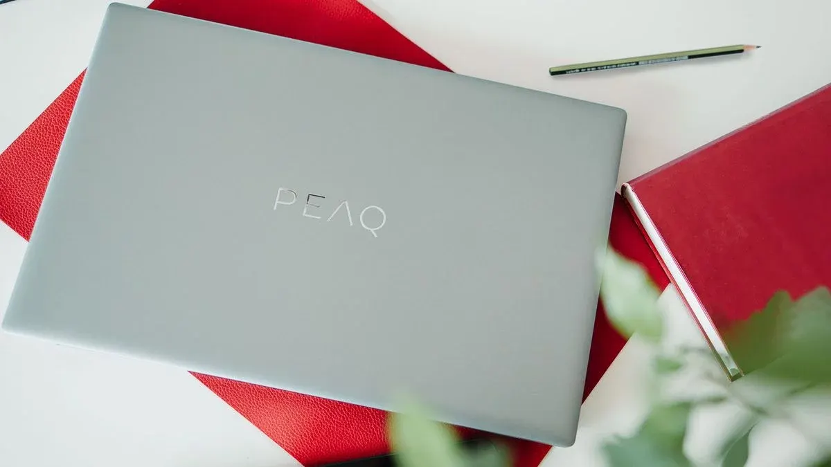 Peaq Laptop liegt auf einem Schreibtisch neben einem Notizbuch und Stift.