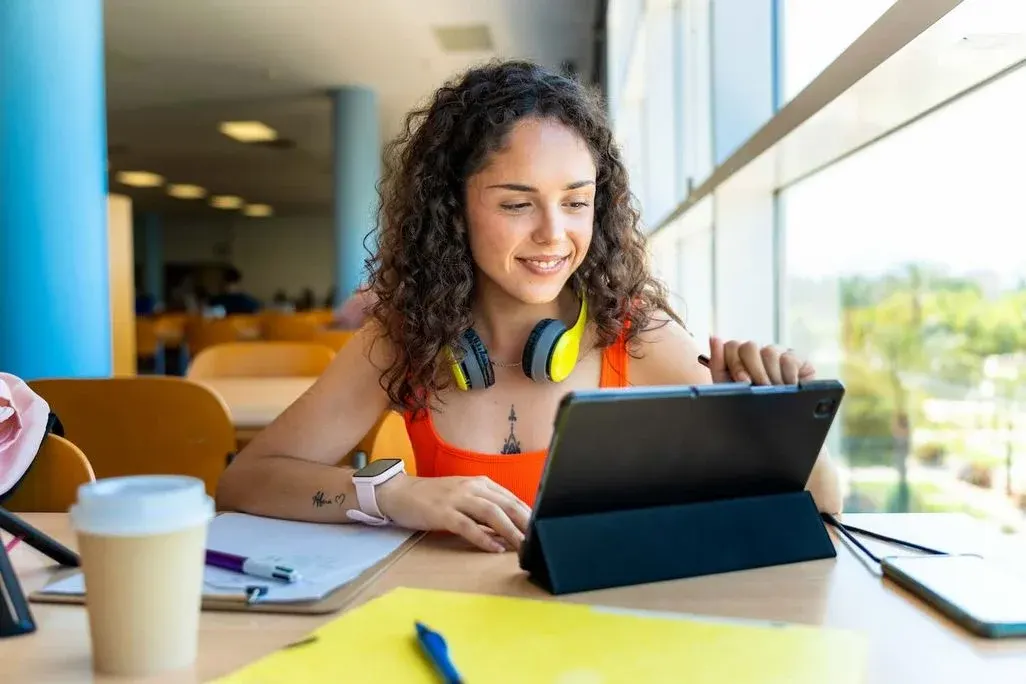 Junge Studentin sitzt mit einem Tablet und Studienunterlagen in einem Hörsaal an einem Tisch.