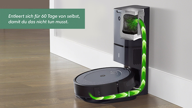 Ein runder, grauer Roboter-Staubsauger steht in einer schwarzen Ladestation an einer weißen Wand. Ein grüner Pfeil zeigt den Saugweg.