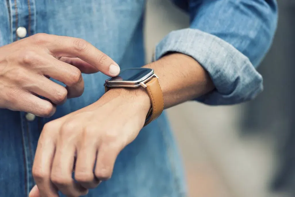 Person im Jeanshemd tippt auf eine Smartwatch mit braunem Lederarmband am Handgelenk.