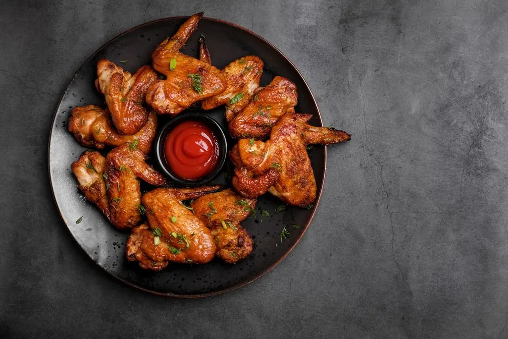 Gebratene Chicken Wings auf einem Teller mit einem Schälchen Ketchup in der Mitte.
