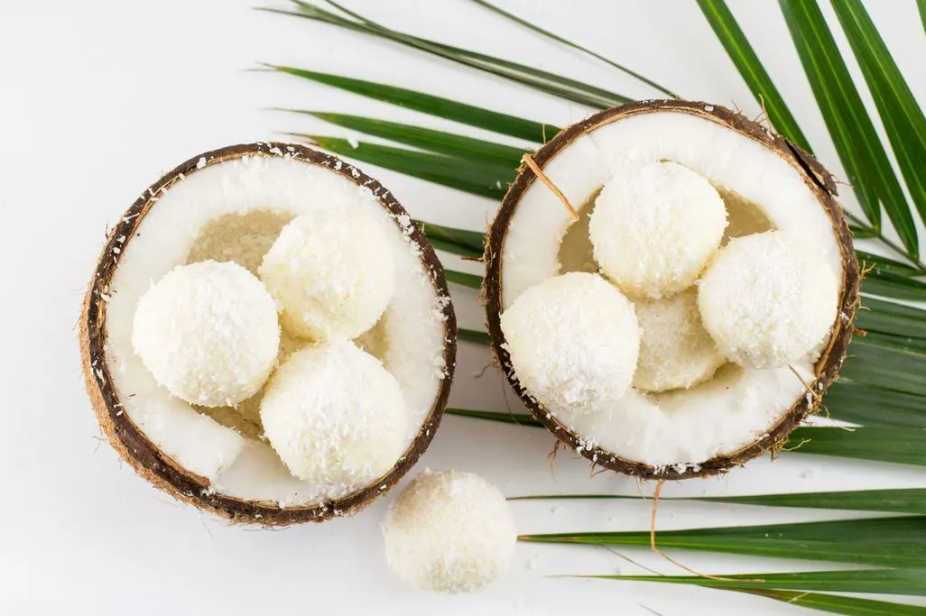 Kokospralinen in einer halbierten Kokosnuss mit Palmenblättern dekoriert.