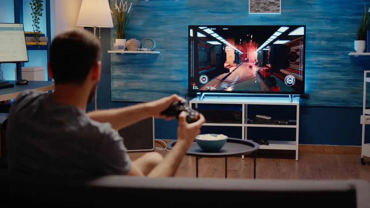 Rote Sci-Fi-Szene auf TV, Person spielt mit Controller auf Sofa. Popcornschale, blauer Raum mit Holzwand, gedämpftes Licht.