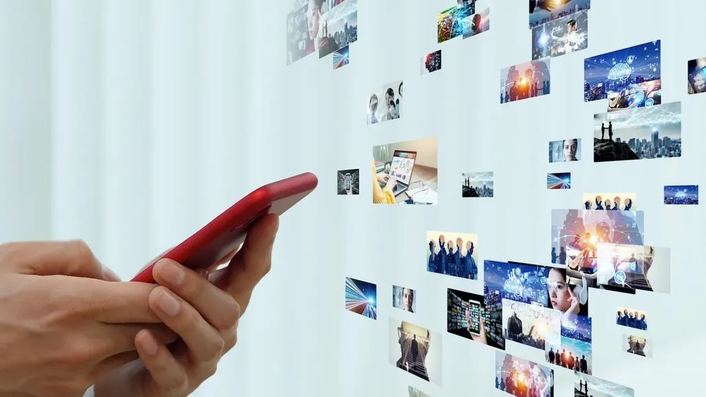 Eine Hand hält ein Smartphone, vor dem zahlreiche digitale Bilder und Videos schweben