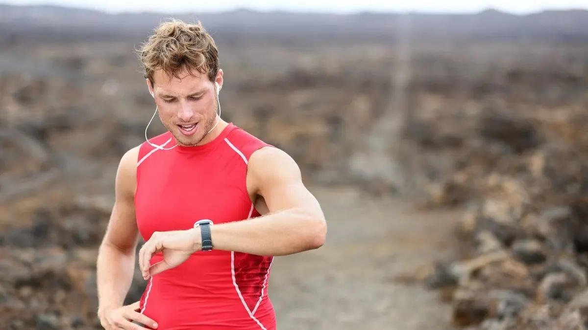 Mann im roten Sportshirt macht eine Pause beim Joggen und schaut auf seine Smartwatch