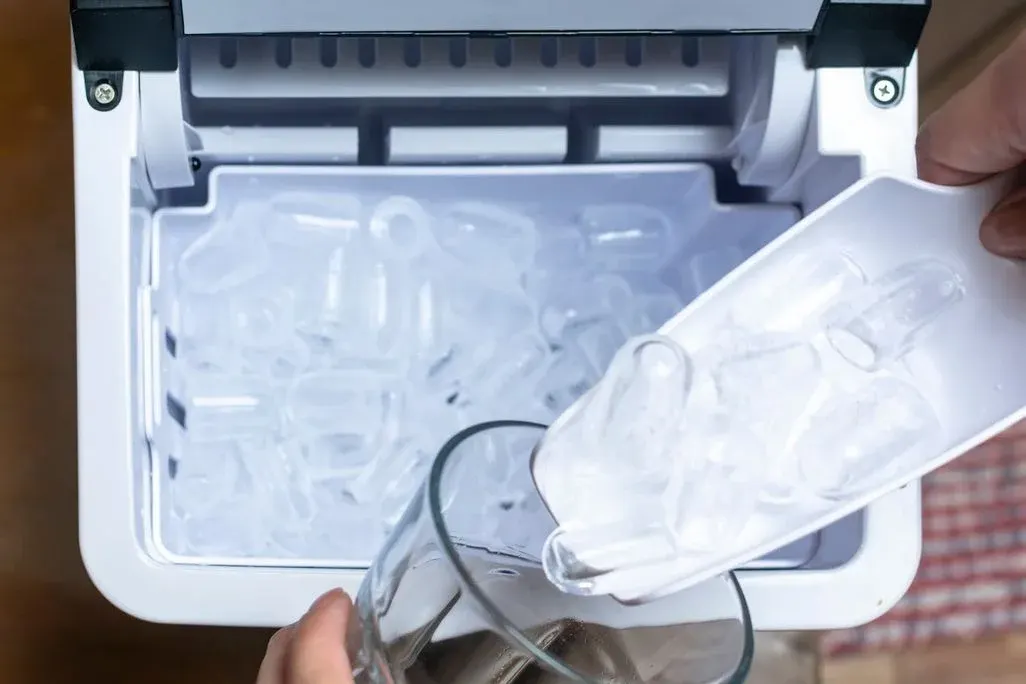 Eiswürfel werden mit einer Schaufel aus einer Eismaschine in ein Glas gefüllt, Nahaufnahme.
