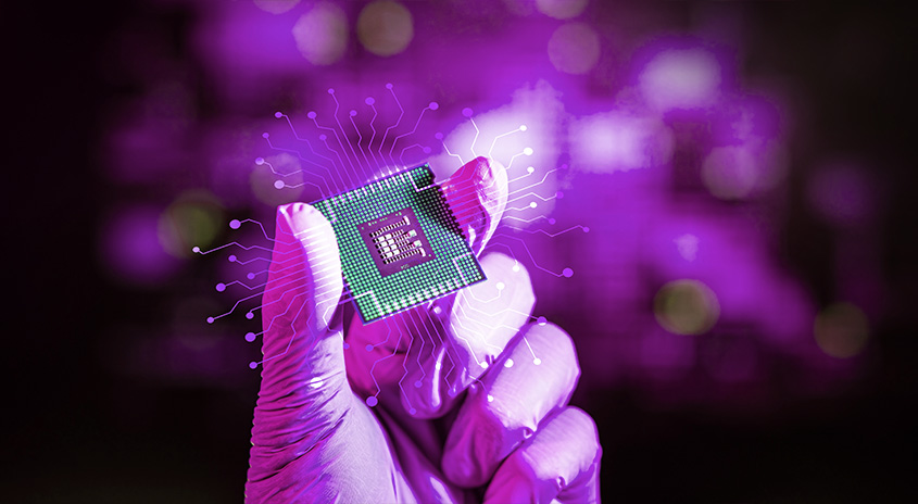 Eine Hand mit Handschuh hält einen grünen Chip vor einem violetten Hintergrund mit Lichtpunkten.