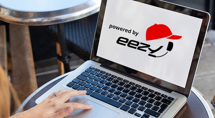 Ein Laptop zeigt ein Logo mit einer roten Kappe und dem Text "powered by eezy". Der Laptop steht auf einem Tisch.