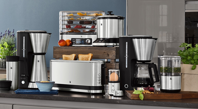 Verschiedene Küchengeräte aus Edelstahl und Schwarz stehen auf einer Küchentheke vor einem blauen Hintergrund.