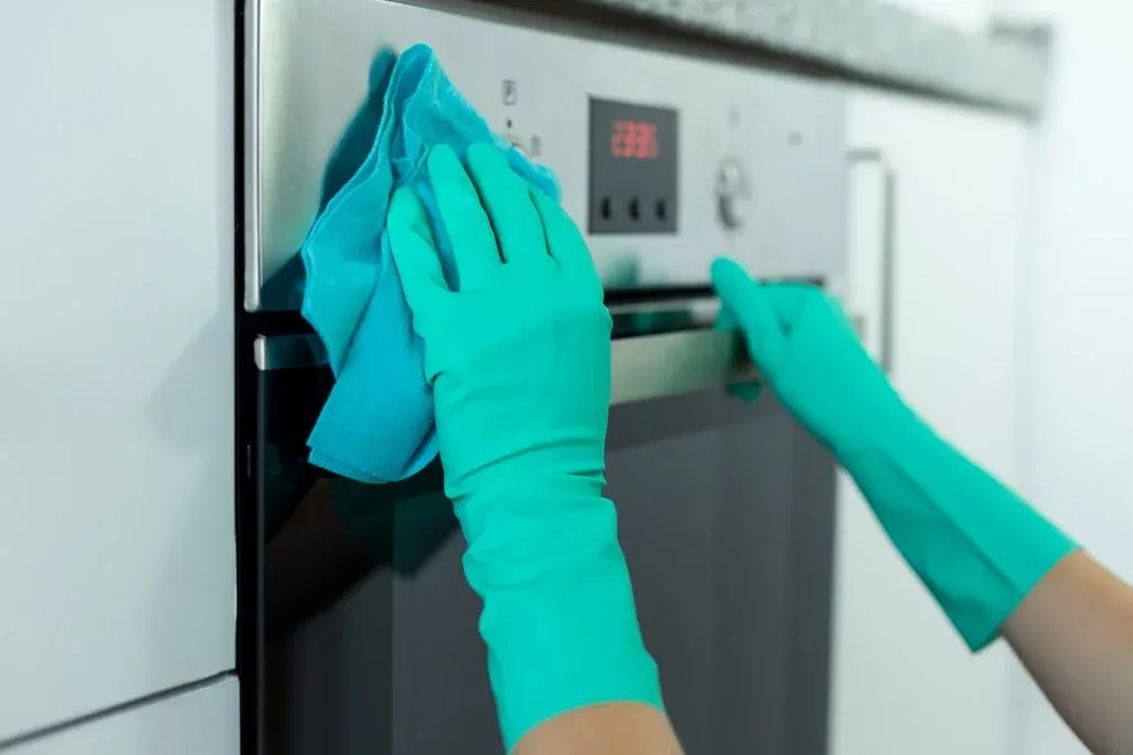 Person mit türkisen Handschuhen reinigt Kühlschrankfront mit Tuch.