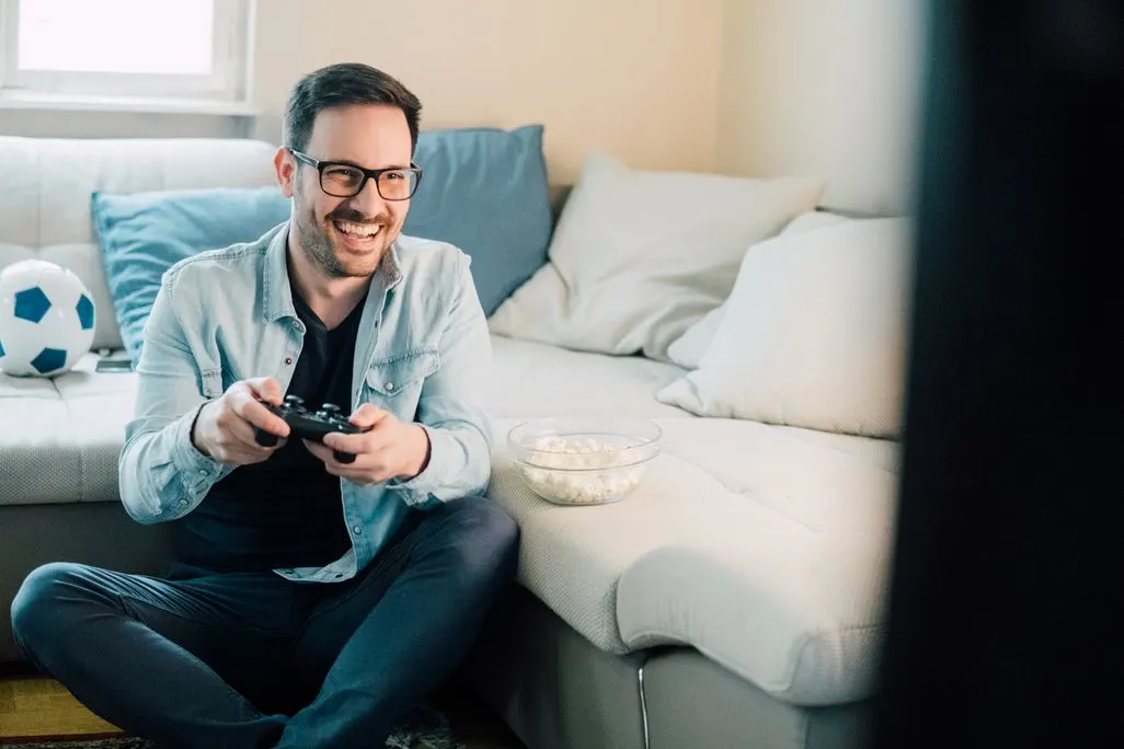 Mann sitzt auf dem Boden vor einem Sofa und spielt mit einem Gamecontroller