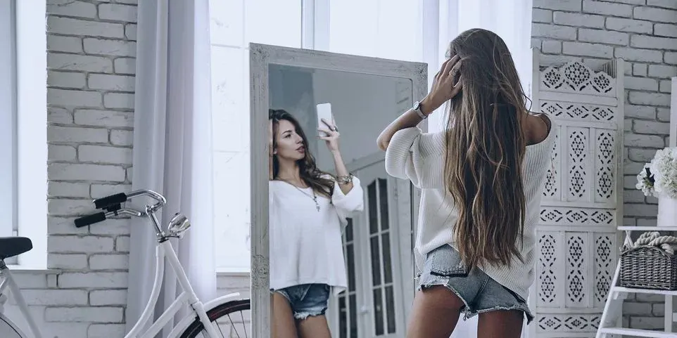Frau mit langem Haar in kurzer Jeansshorts macht ein Selfie vor dem Spiegel.