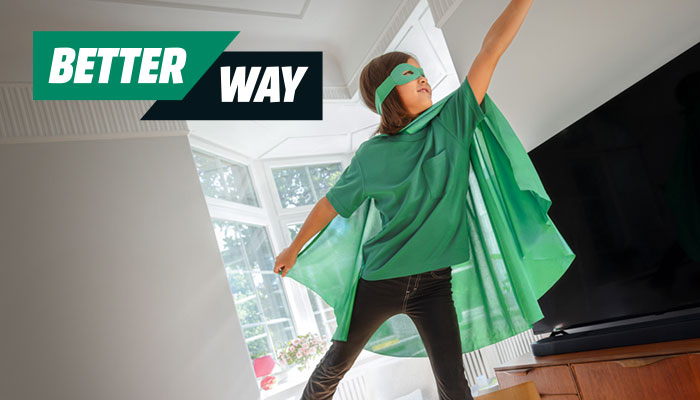 Ein Kind mit grüner Maske und Umhang steht in einem Raum mit Fernseher und Fenstern.