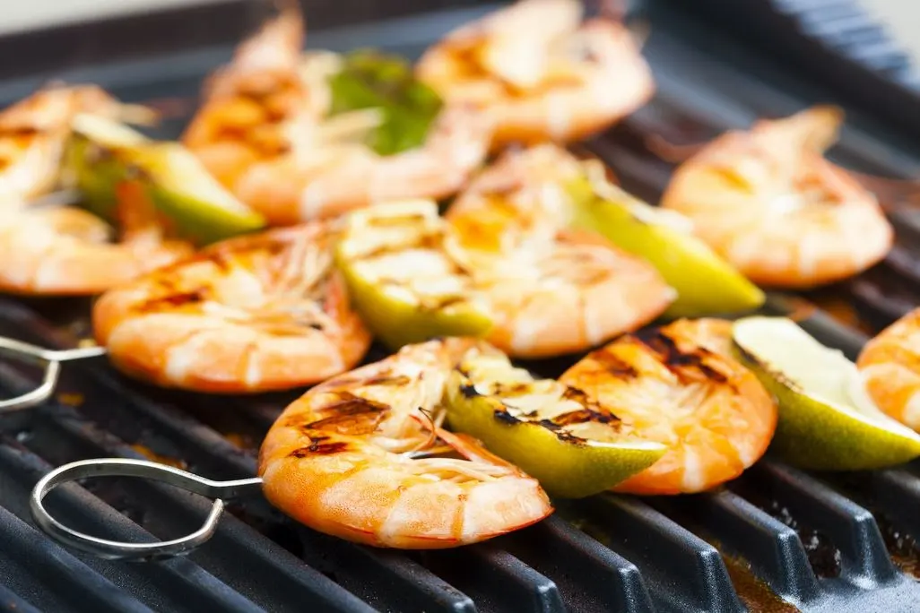 Garnelen und Limettenstücke auf Spießen werden auf einem Grill gegart.