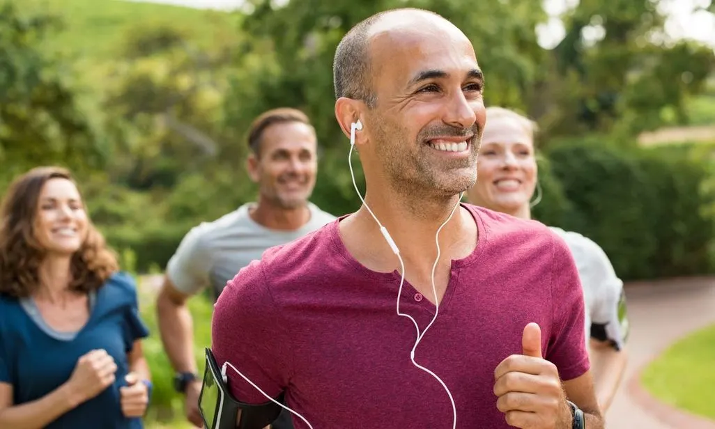 Ein lächelnder Jogger mit In-Ear-Kopfhörern, im Hintergrund drei weitere Jogger.