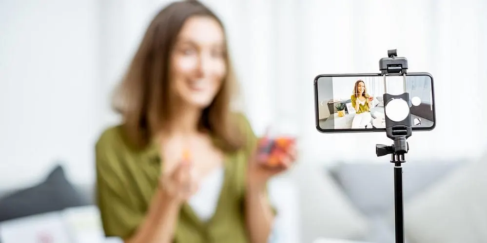 Eine Frau filmt sich selbst mit einem Smartphone und präsentiert einen bunten Gegenstand.