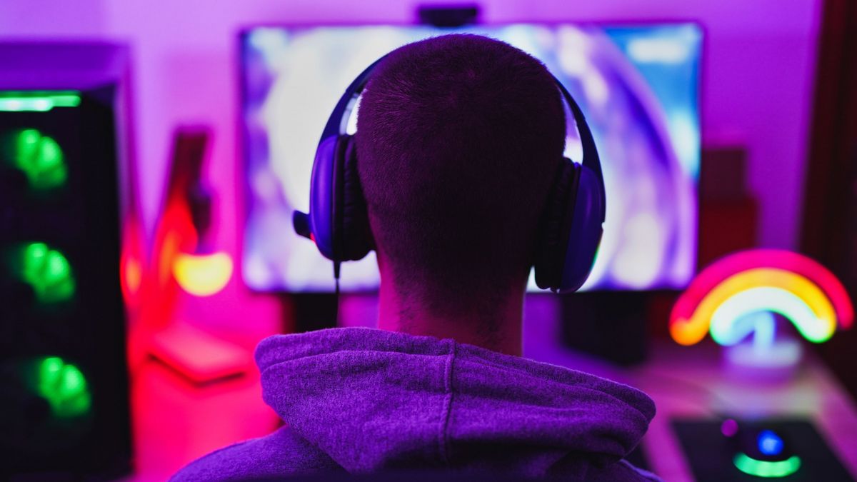 Ein Mann mit Kophörern sitzt vor einem Monitor in einem bunt beleuchteten Gaming Zimmer