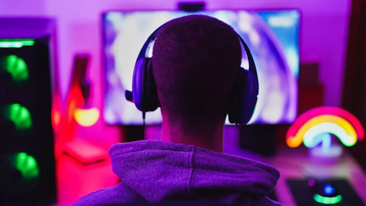 Ein Mann mit Kophörern sitzt vor einem Monitor in einem bunt beleuchteten Gaming Zimmer