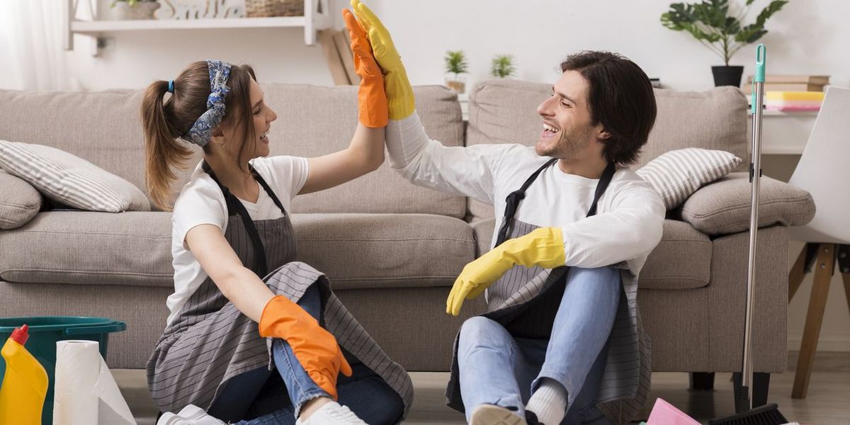 Zwei Personen sitzen in einem Wohnzimmer und geben sich ein High Five beim gemeinsamen Putzen.