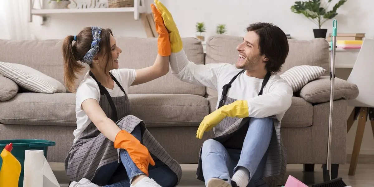 Zwei Personen sitzen in einem Wohnzimmer und geben sich ein High Five beim gemeinsamen Putzen.
