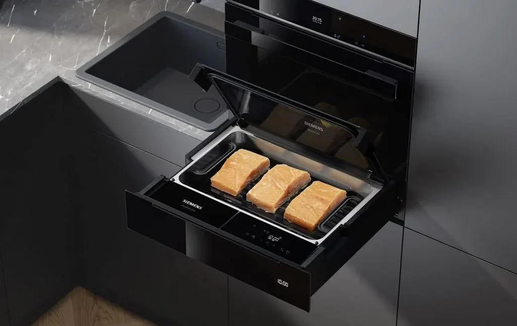 Drei Lachsfilets auf einem Grillrost in einem geöffneten Siemens Dampfgarer. Dunkle Küche mit schwarzer Spüle und Digitalanzeigen.
