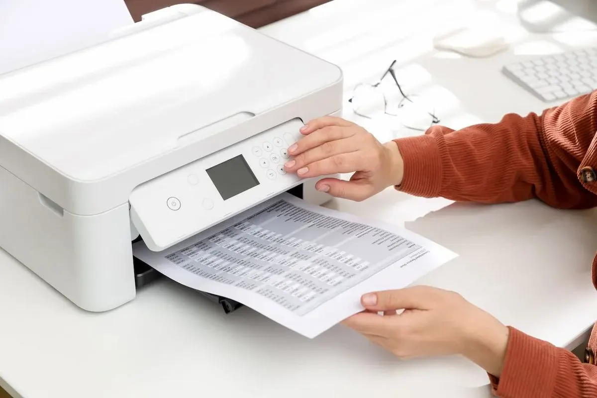 Hand bedient weißen Drucker; gedrucktes Blatt mit Tabellendaten wird herausgezogen.